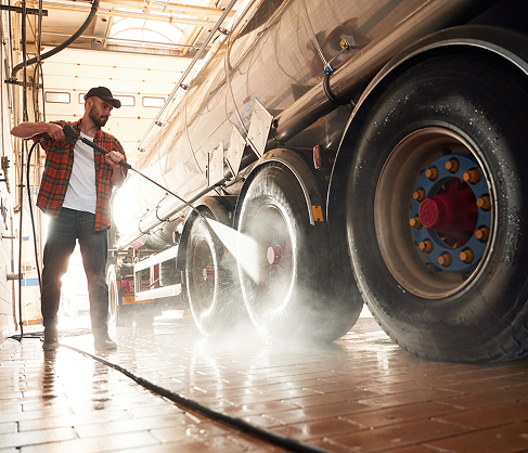 Worker cleaning large vehicle with hose